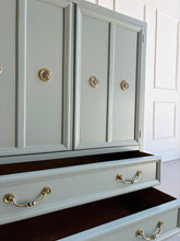 Load image into Gallery viewer, This vintage Thomasville armoire professionally lacquered in a custom muted green with soft blue-gray undertones, while the interior is finished in French Roast. Four paneled doors open to reveal divided upper compartments and two pull-out tray drawers. Two spacious lower drawers offer additional concealed storage. Good Bones Furniture
