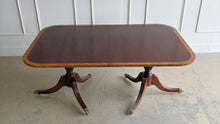 Load image into Gallery viewer, Classic proportions and refined craftsmanship give this vintage banded mahogany dining table its timeless appeal. The rich mahogany top is framed by a contrasting banded edge that adds subtle visual definition, while the double pedestal base brings balance, elegance, and stability. Carved pedestal details and brass-capped feet. Good Bones Furniture
