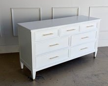 Load image into Gallery viewer, This vintage dresser by Kindel Furniture blends heirloom craftsmanship with a fresh, tailored update. Professionally lacquered in Benjamin Moore White Dove, the finish gives the piece a soft, warm white presence that feels crisp without feeling stark. Fluted corner posts add subtle classical detail, while slim brass bar pulls and brass-capped feet introduce a refined modern contrast. Good Bones Furniture
