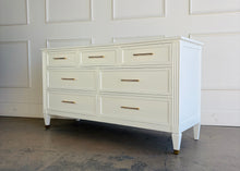 Load image into Gallery viewer, This vintage dresser by Kindel Furniture blends heirloom craftsmanship with a fresh, tailored update. Professionally lacquered in Benjamin Moore White Dove, the finish gives the piece a soft, warm white presence that feels crisp without feeling stark. Fluted corner posts add subtle classical detail, while slim brass bar pulls and brass-capped feet introduce a refined modern contrast. Good Bones Furniture
