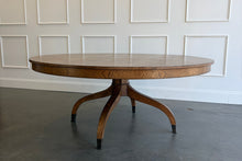 Load image into Gallery viewer, The Williamsburg Dining Table combines dramatic wood grain with a graceful, sculptural base. Crafted from mahogany solids, its expansive round top is available in your choice of richly figured burled ash or cerejeira veneer. Carefully arranged veneer panels create movement across the tabletop, while the substantial veneered apron adds visual depth. Four sweeping legs extend from the central pedestal and terminate in brass-capped feet. Good Bones Furniture

