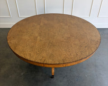 Load image into Gallery viewer, The Williamsburg Dining Table combines dramatic wood grain with a graceful, sculptural base. Crafted from mahogany solids, its expansive round top is available in your choice of richly figured burled ash or cerejeira veneer. Carefully arranged veneer panels create movement across the tabletop, while the substantial veneered apron adds visual depth. Four sweeping legs extend from the central pedestal and terminate in brass-capped feet. Good Bones Furniture
