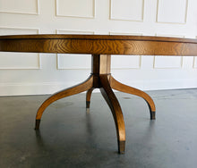 Load image into Gallery viewer, The Williamsburg Dining Table combines dramatic wood grain with a graceful, sculptural base. Crafted from mahogany solids, its expansive round top is available in your choice of richly figured burled ash or cerejeira veneer. Carefully arranged veneer panels create movement across the tabletop, while the substantial veneered apron adds visual depth. Four sweeping legs extend from the central pedestal and terminate in brass-capped feet. Good Bones Furniture
