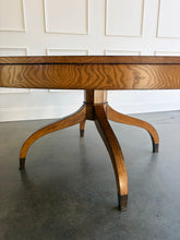 Load image into Gallery viewer, The Williamsburg Dining Table combines dramatic wood grain with a graceful, sculptural base. Crafted from mahogany solids, its expansive round top is available in your choice of richly figured burled ash or cerejeira veneer. Carefully arranged veneer panels create movement across the tabletop, while the substantial veneered apron adds visual depth. Four sweeping legs extend from the central pedestal and terminate in brass-capped feet. Good Bones Furniture
