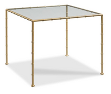 Load image into Gallery viewer, This amazing showroom sample is in like new condition. Channeling the sophistication of 19th-century English Regency design, the Lacoste Game Table adds a touch of timeless glamour to any setting. Its square top is inset with 3/8" tempered glass, offering both clarity and durability, while the frame and legs—cast in brass with faux bamboo turning—bring subtle ornamentation and a warm golden glow.
