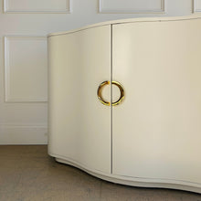 Load image into Gallery viewer, Close-up detail of brass half-moon pulls on the Highland House Jules Cabinet, highlighting the smooth creamy white lacquer and curved cabinet front.
