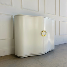 Load image into Gallery viewer, Angled view of the Highland House Jules Cabinet showing its gently bowed front, rounded edges, and creamy white lacquer finish with brass half-moon hardware by Good Bones Furniture.
