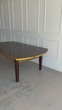 Load and play video in Gallery viewer, Theodore Alexander Sebastiano Dining Table pairs a historic silhouette with a modern, tailored edge. Its gently curved rectangular top is framed by a brass-bound apron that gives the piece a crisp, architectural presence, while slatted baluster legs outlined in gilt add depth and refinement. Open box showroom sample. Good Bones Furniture
