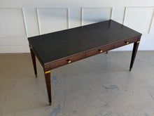 Load image into Gallery viewer, Wide 45-degree downward angled view from the right of the Theodore Alexander Bradbury Desk, highlighting the khaya swirl wood top, tapered legs, and brass hardware at Good Bones Furniture in Raleigh, NC.
