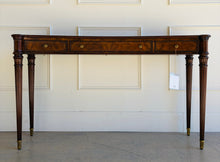 Load image into Gallery viewer, Front view of the Theodore Alexander Grandinson Console featuring richly finished mahogany, refined classical detailing, and brass accents, photographed in a bright showroom setting.
